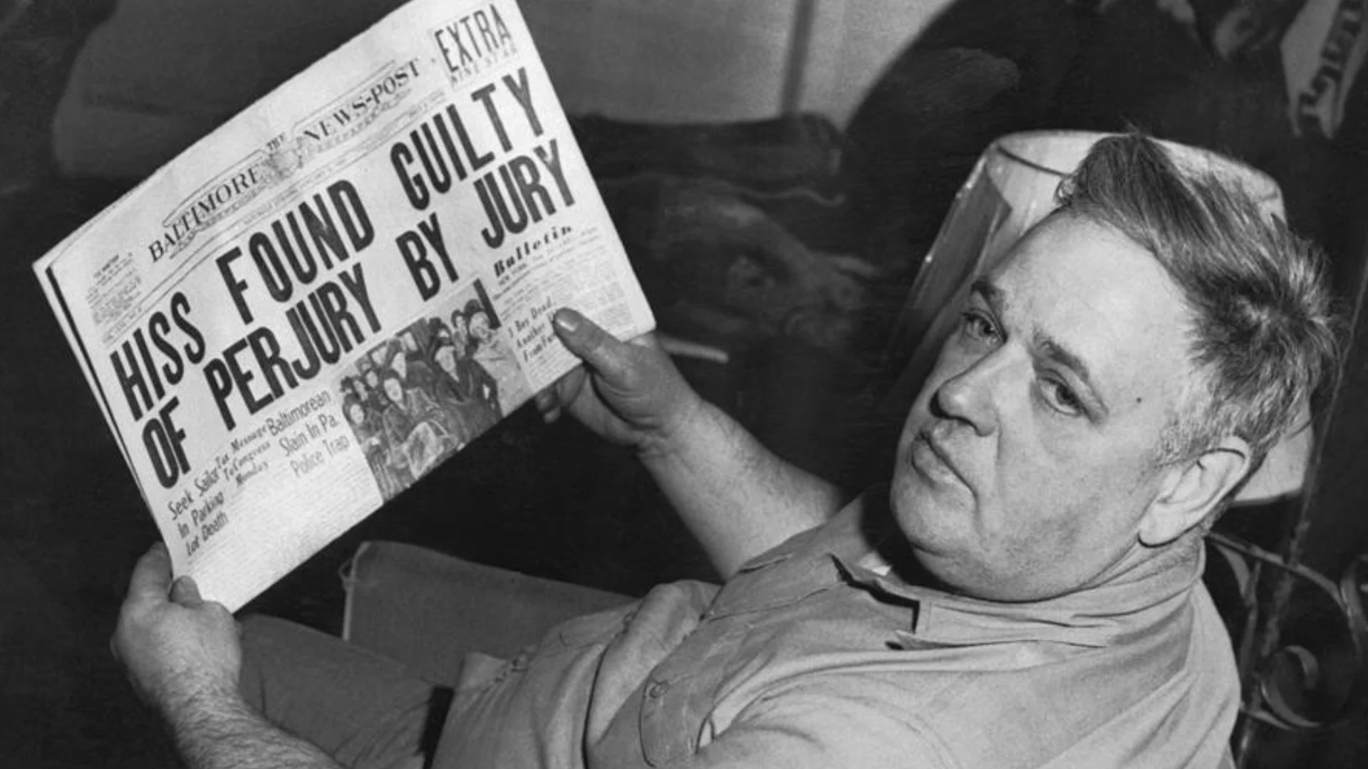 Man sitting and reading a newspaper with the bold headline 'Hiss found guilty of perjury' in a black-and-white photo