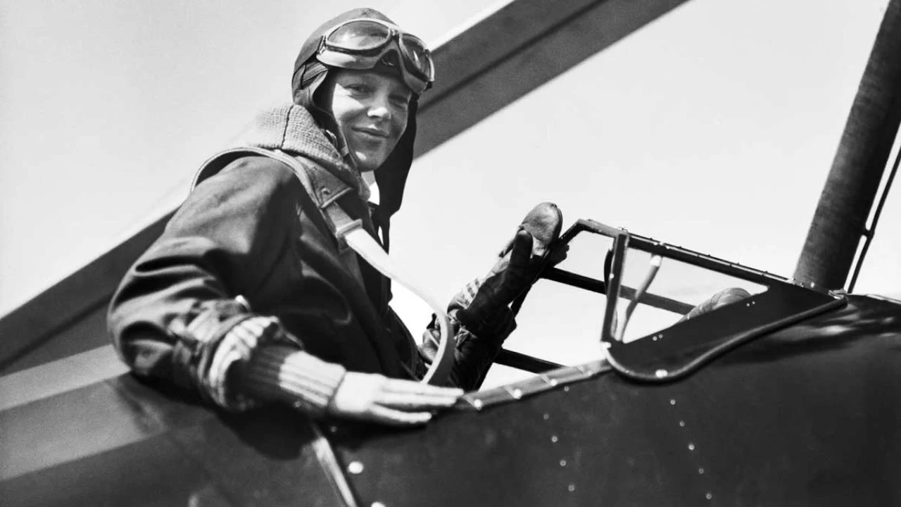 Pilot in vintage flight gear, wearing goggles and a leather jacket, prepares to enter an open cockpit aircraft.
