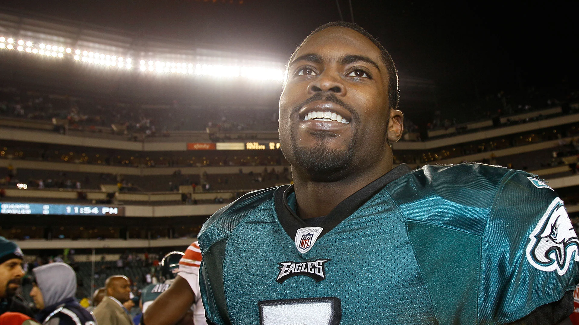 Close-up of a smiling African American football player in an Eagles jersey on the field at night stadium.